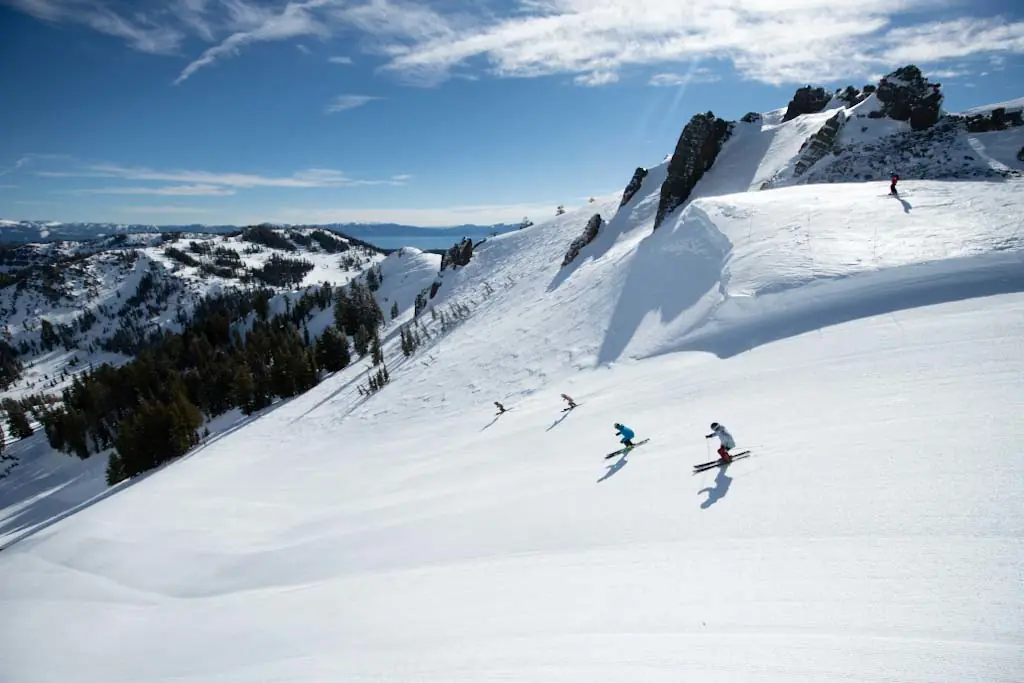 skiers descending a groomed run on a sunny day in Palisades Tahoe, California