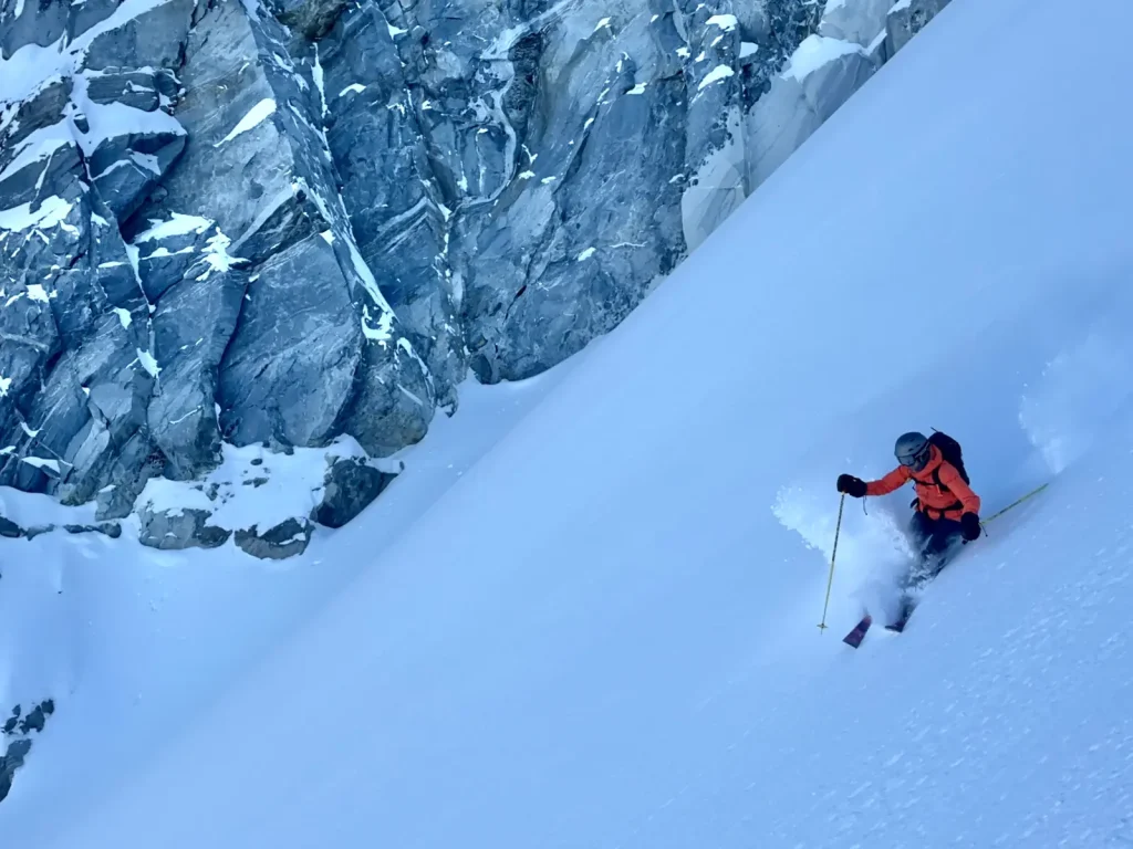 heli skier descending a steep chute in powder